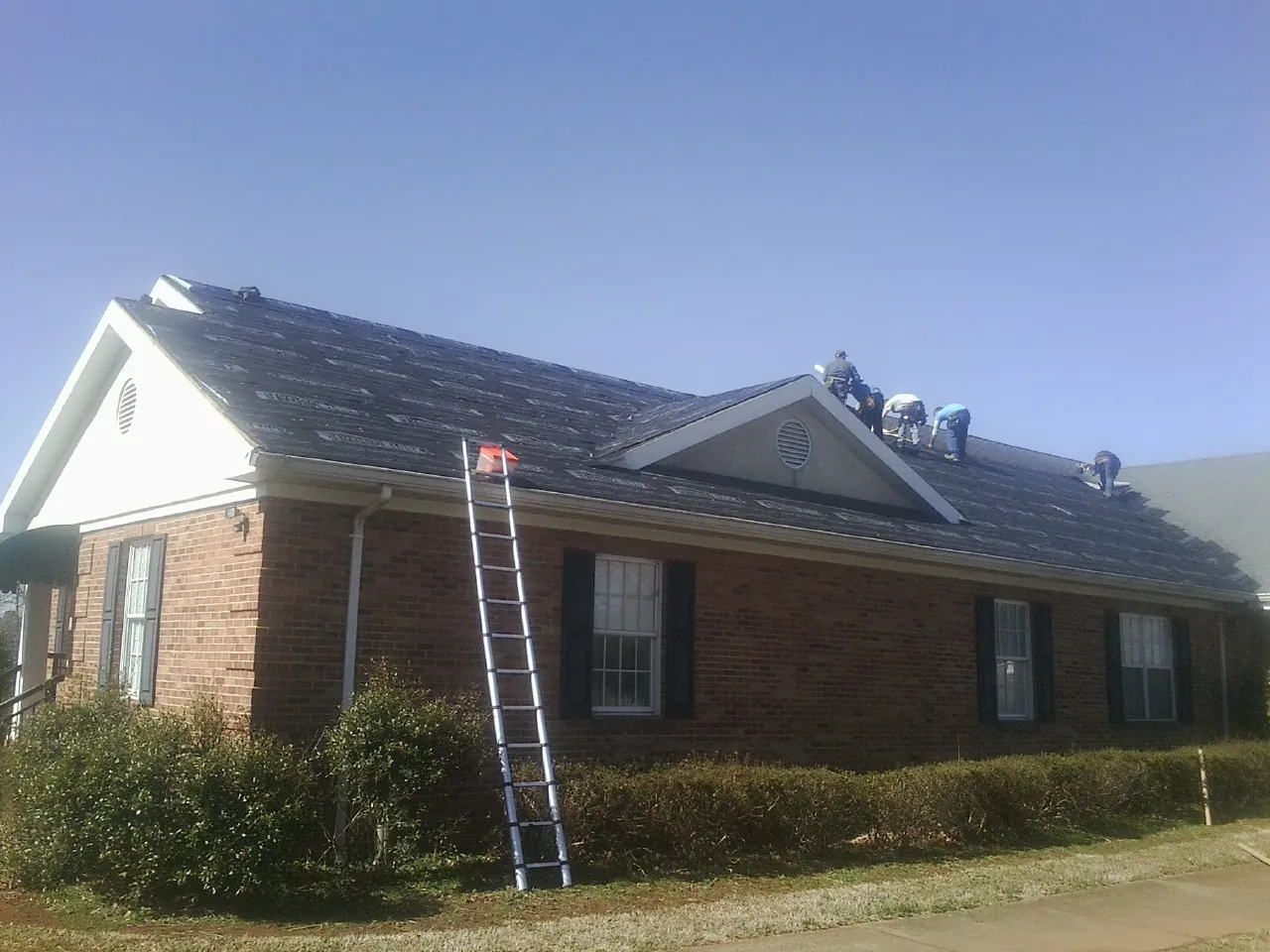 Crew tearing shingles off a brick ranch roof with a ladder set — Emergency Roof Repair work by our crew in Sabula