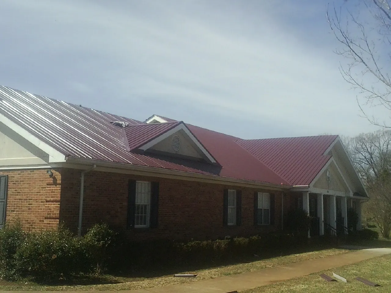 Red metal roof with gabled entries on a long brick building, from a Hail Damage Roof Repair job in Sabula