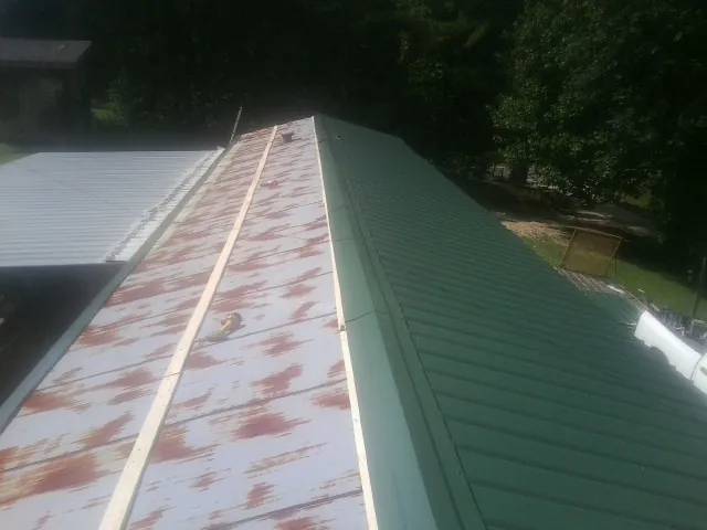 Old rusted panels beside newly installed green metal roofing — Wind Damage Roof Repair by Roofing Brothers in Sabula