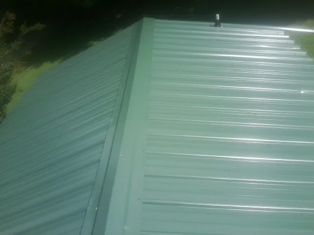 New green metal panels meeting at the ridge of a roof — Flat Roof Repair work by our crew in Sabula