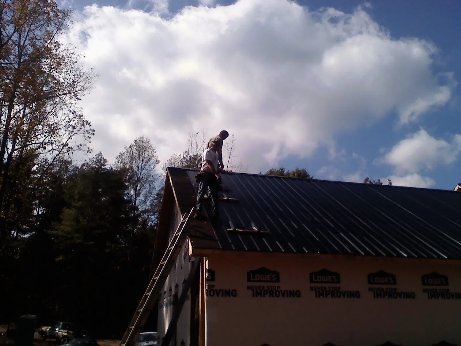 Roofer fastening dark metal panels high against a cloudy sky, from a Roof Inspection job in Sabula