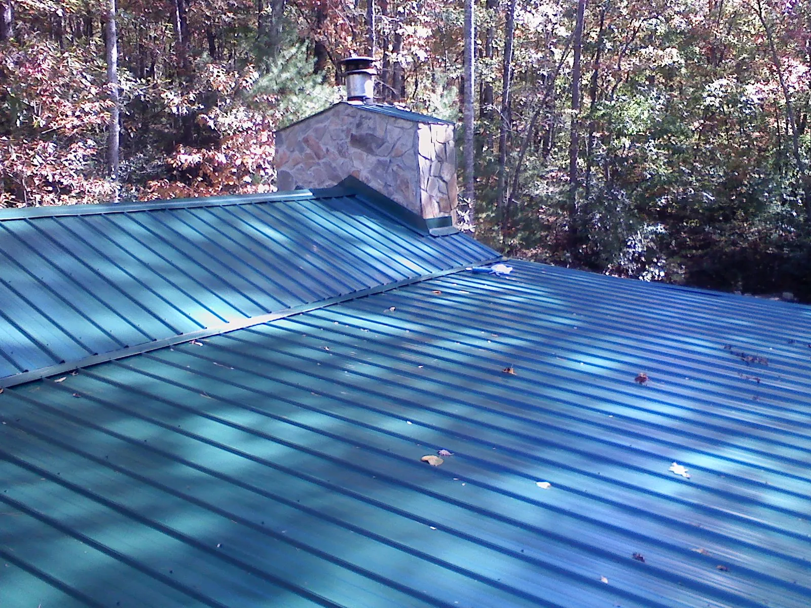 New green metal roof and stone chimney surrounded by autumn woods in Sabula
