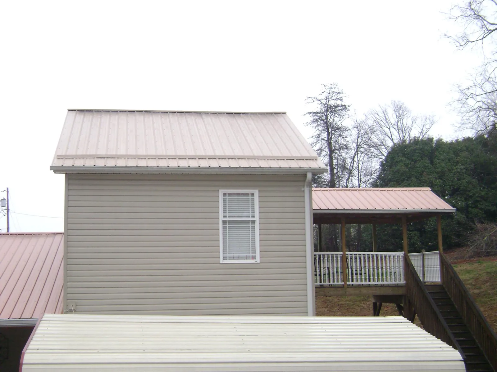 Tan metal roofs on a two story addition and attached porch, from a Roof Replacement job in Sabula